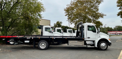 Tow truck flatbed showing Kenworth T280 cab and flatbed with multiple auxiliary tow trucks in background.