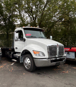 Kenworth T280 tow truck front left view showing white cab and chrome grille with 2025 sticker on windshield