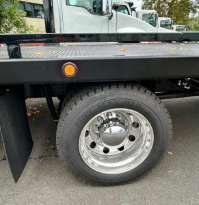 Tow truck wheel and chassis side view showing chrome center cap, polished steel wheel, tire, and black steel frame with amber marker light.