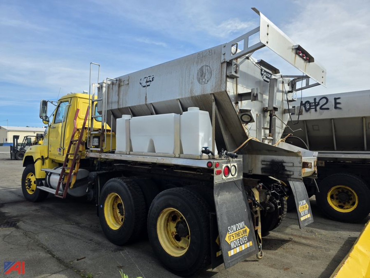 Western Star 4700 chassis with stone spreader attachment, dual rear axles, yellow wheels, white plastic tanks on bed, and metal stinger at rear.