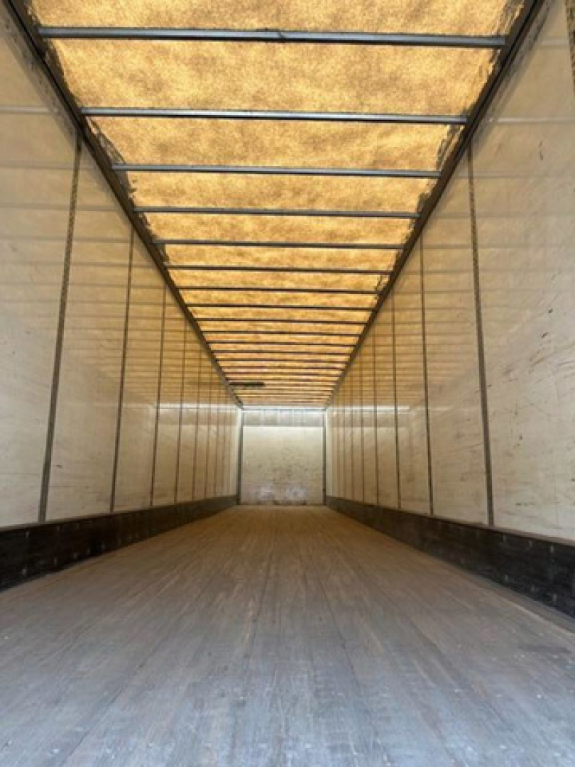 Van trailer interior showing long empty cargo space with wooden ceiling supports and side walls.
