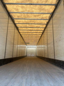 Van trailer interior showing long empty cargo space with wooden ceiling supports and side walls.