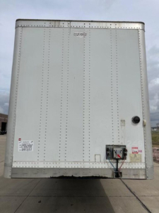 Rear view of a white 2014 Wabash van trailer showing back doors, riveted panels, corner binding, and a hitch/tongue area with labels.