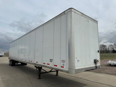 Trailer van showing exterior side and front corner with wheel, reflective striping, and hitch area.
