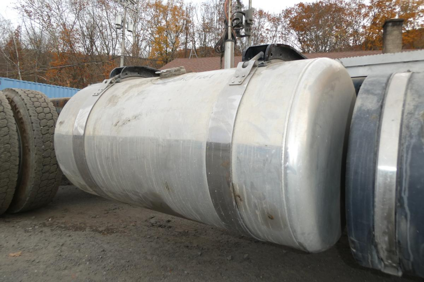 Tank or cylindrical fuel/air reservoir lying horizontally on ground, metallic with hinge straps on top, part of a Peterbilt 567 truck in a yard.