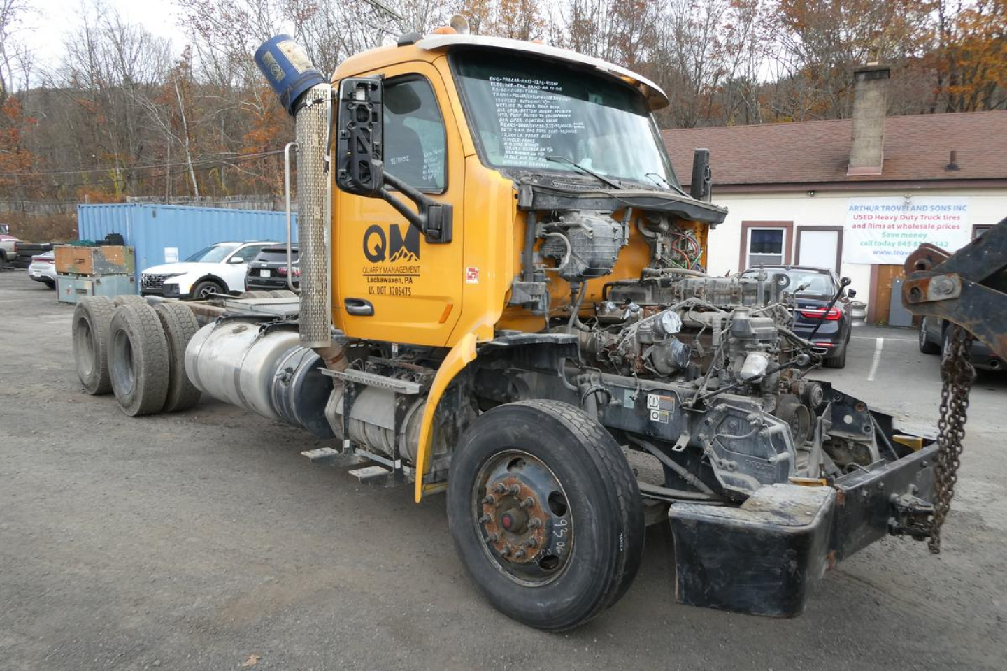 Truck chassis with cab detached showing engine bay and exposed components in yard.