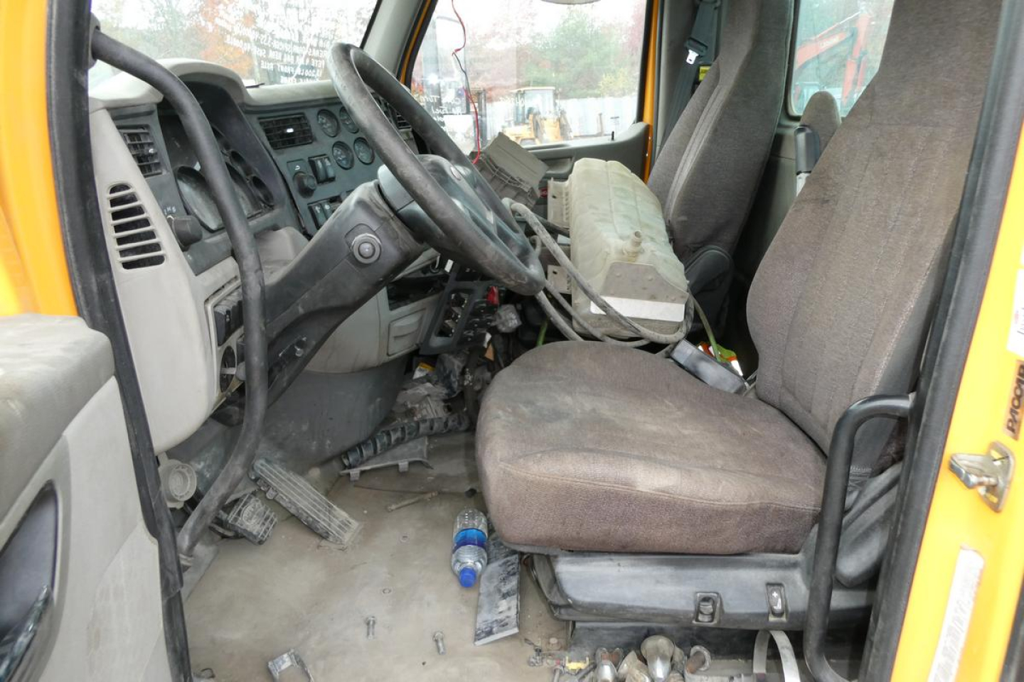 Peterbilt 567 cab interior view showing driver’s seat, steering wheel, dashboard, and worn floor mat with scattered debris.