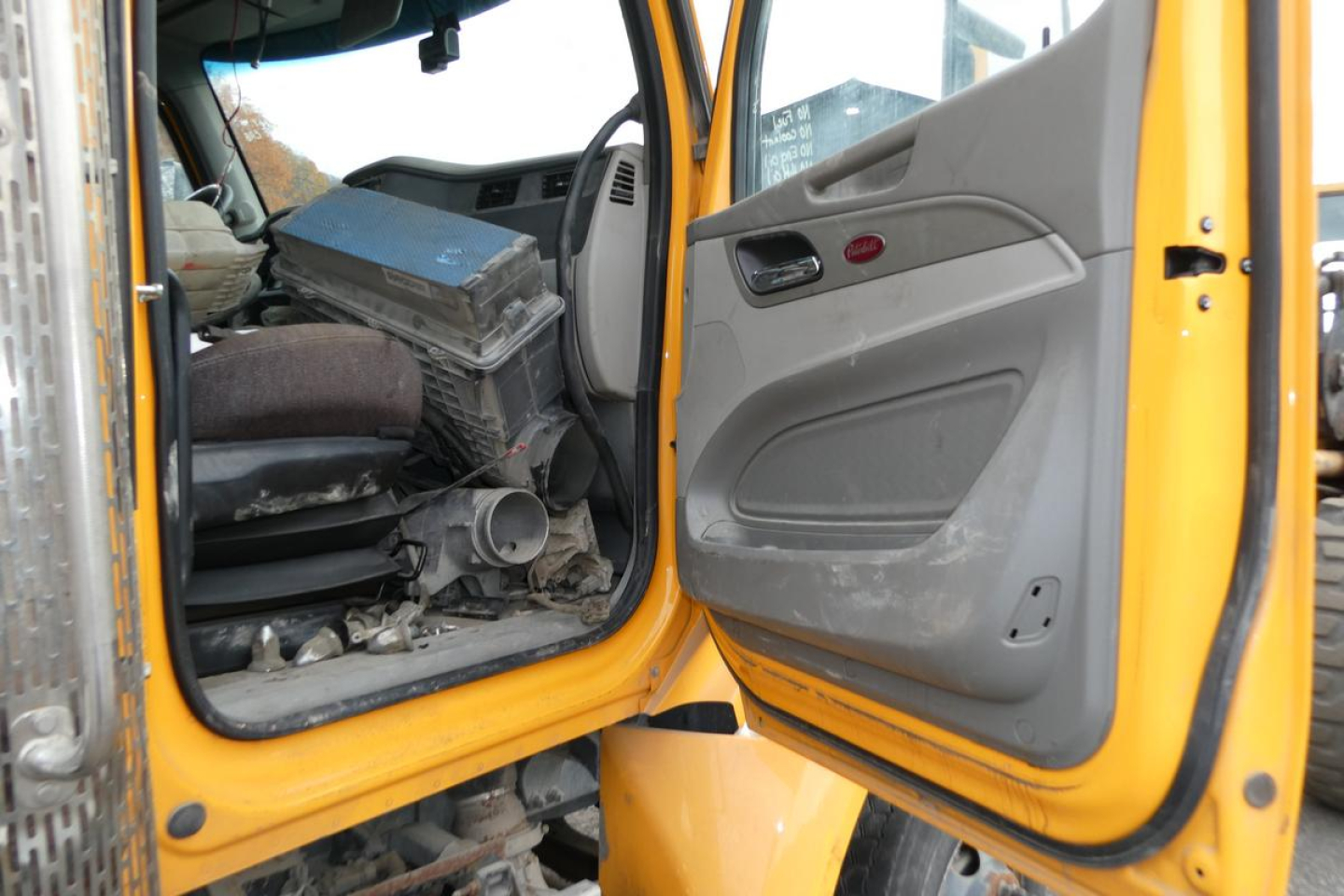 Peterbilt 567 cab interior view showing open door and driver seat area with dashboard and debris inside.
