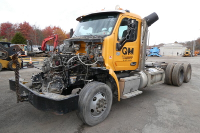 Truck cab and chassis of a 2019 Peterbilt 567 with exposed engine bay, front end off, orange cab, wheels, and exposed wiring.