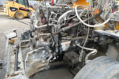 Peterbilt 567 engine bay showing exposed drivetrain with hoses, metal brackets, and wiring harnesses; partial cab removed exposing components.