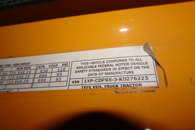 Vehicle label showing compliance text and VIN plate on orange Peterbilt 567, with VIN 1XPCDP9X3KD276225 and federal safety standards information.