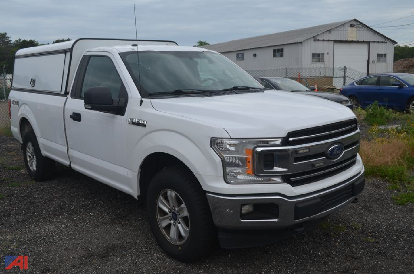 Ford F-150 pickup truck with white paint and a camper shell in a lot.