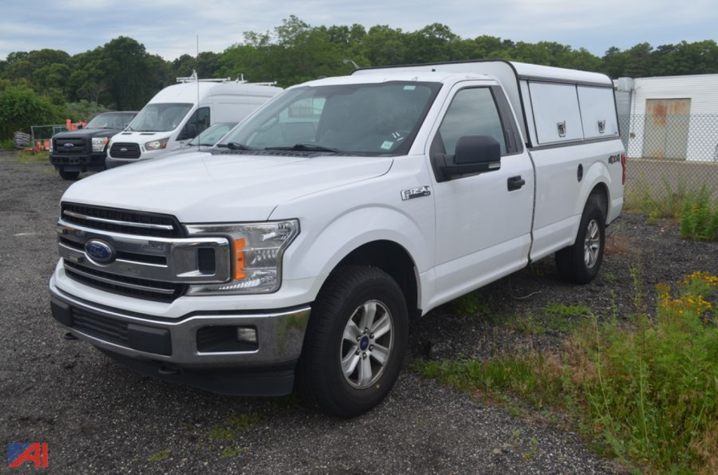 Ford F-150 pickup truck in white with utility camper shell in a dealership lot.