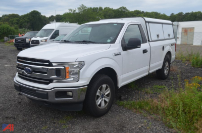 Ford F-150 pickup truck in white with utility camper shell in a dealership lot.
