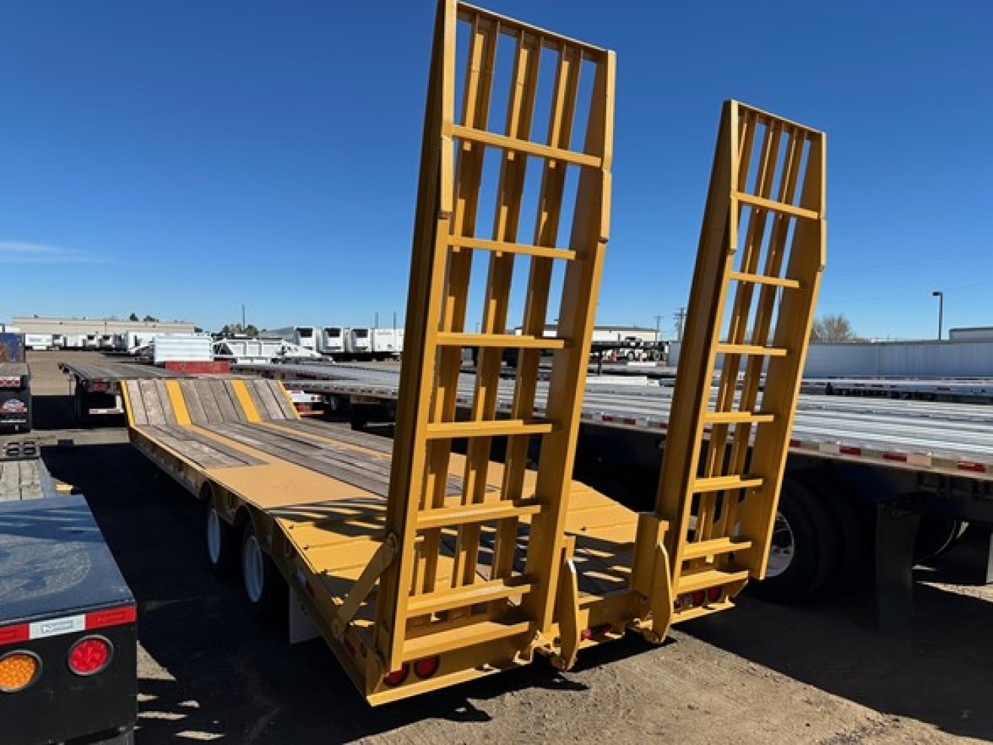 Trailer showing yellow 20-ton equipment trailer with hydraulic air ramps, rear loading ramps raised, tandem axles, flatbed with guard rails.