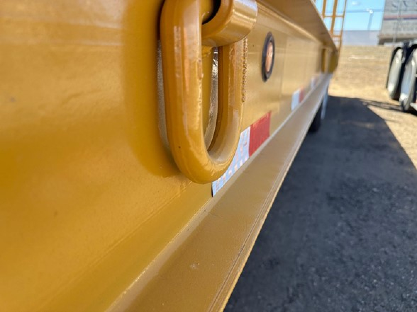 Trailer side showing yellow paint, D.O.T. safety ring and reflective strips on a lowboy trailer with hydraulic air ramps.