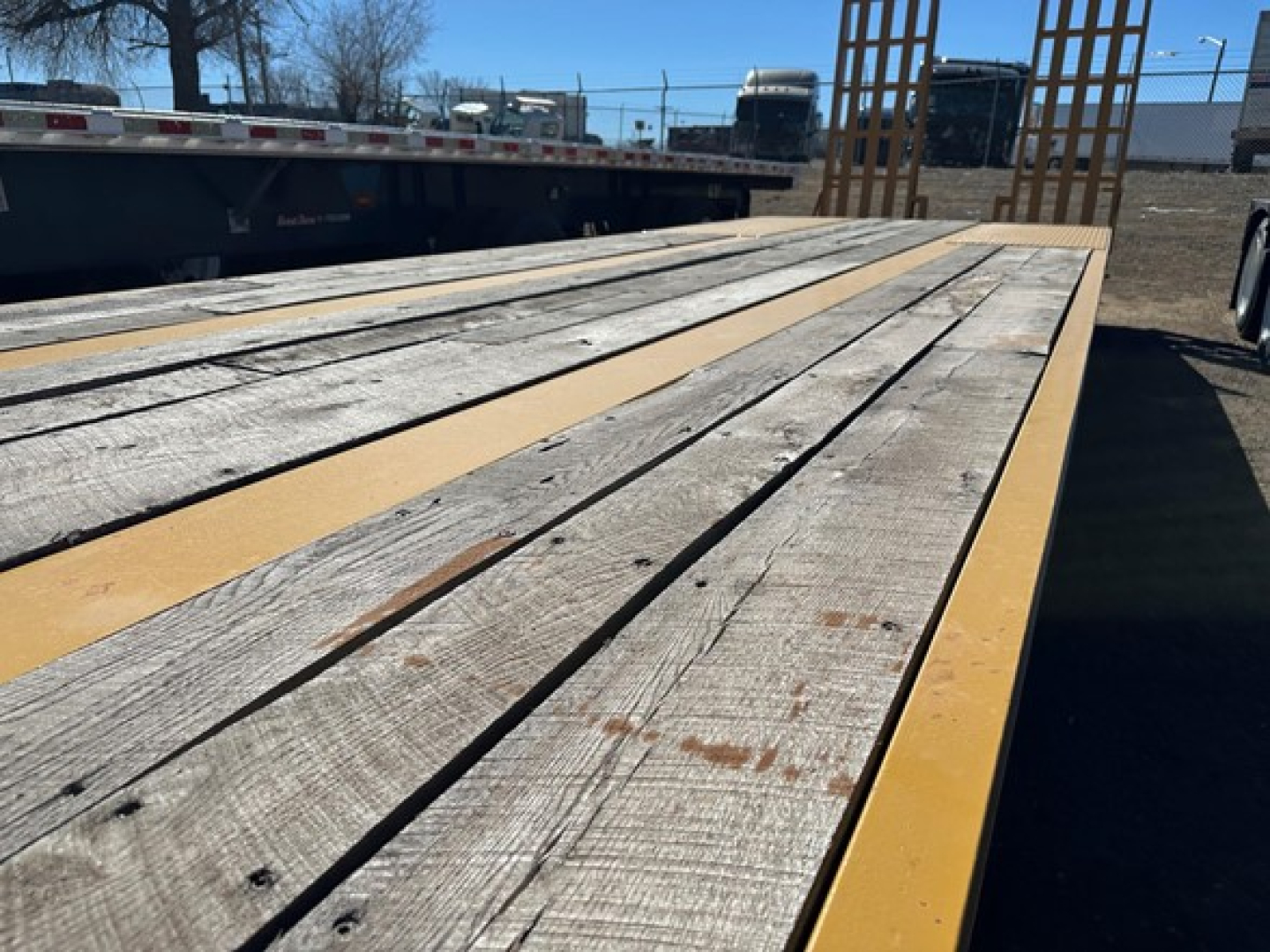 Trailer deck with wooden planks and yellow edge rails, flatbed cargo trailer viewed from front-left, lowboy configuration.