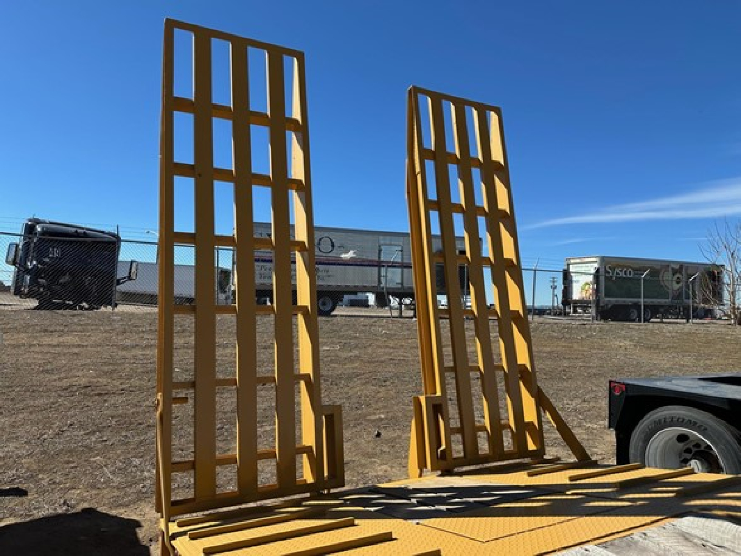 Trailer with hydraulic air ramps in yellow, two tall ramp structures standing upright on a lowboy trailer, clear blue sky.