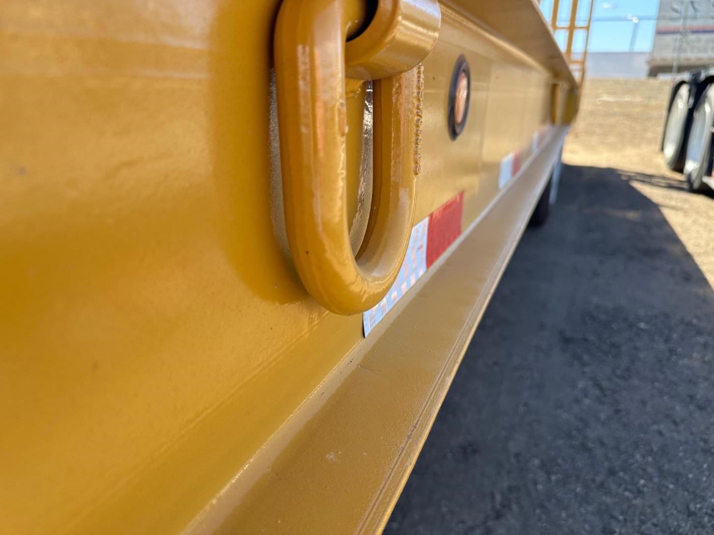 Trailer side with a yellow ring latch and reflective strip, close-up showing a D-shape handle and white/red caution sticker along the lower edge.