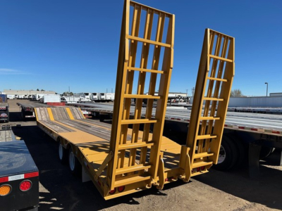Trailer showing yellow 20-ton equipment trailer with hydraulic air ramps, rear loading ramps raised, tandem axles, flatbed with guard rails.