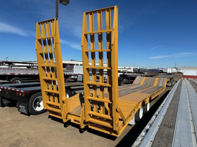 Equipment trailer with two vertical loading ramps on a lowboy trailer, yellow paint, long platform, in outdoor lot.
