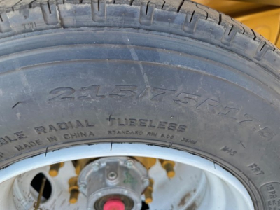 Trailer wheel and tire close-up showing radial tubeless tire with tread, wheel rim, and part of the trailer frame in yellow. Visible text on tire includes 215/75R17.5 and MADE IN CHINA STANDARD RD 00 JRN.