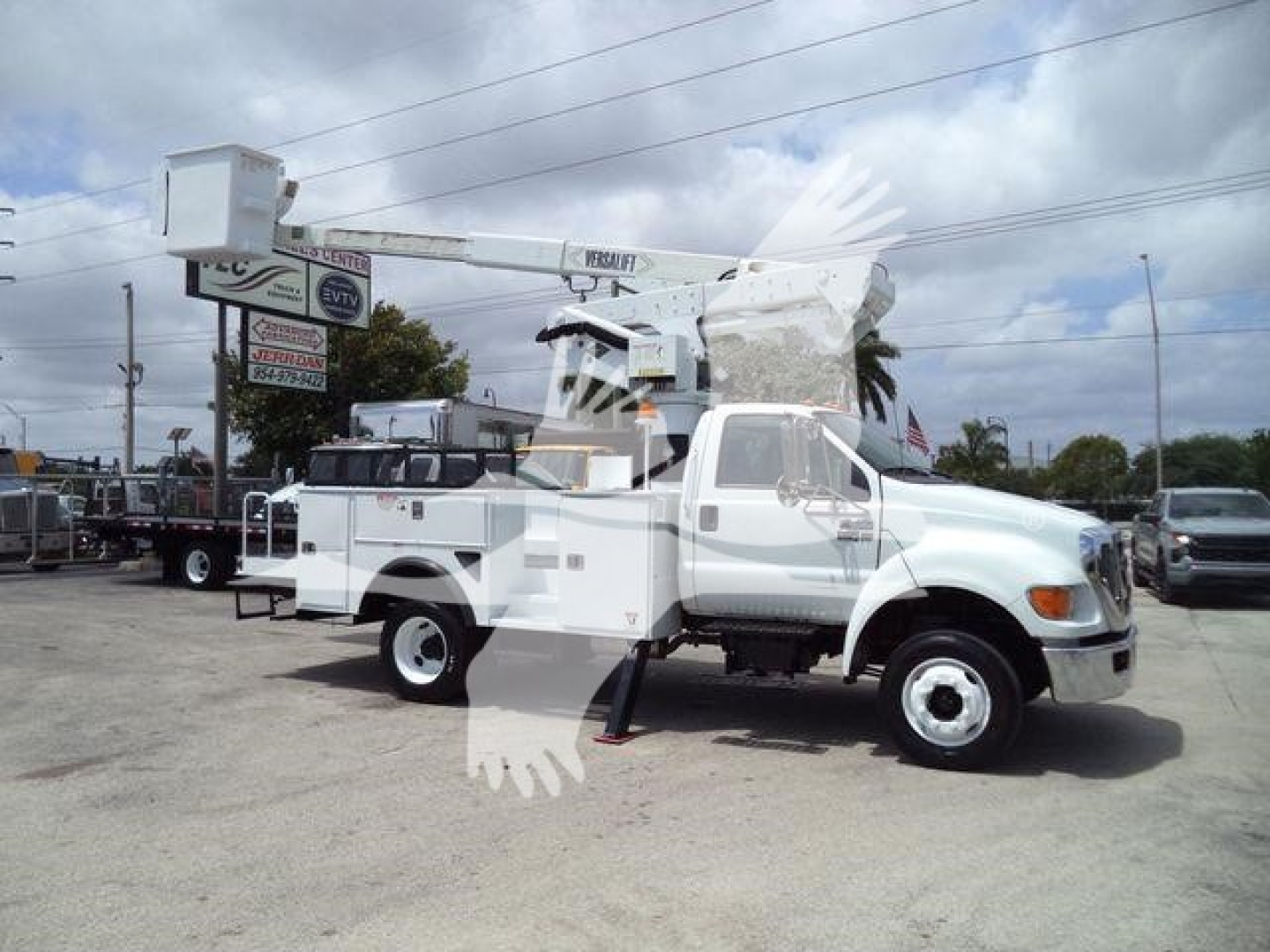Versalift VST40i bucket crane mounted on a white truck chassis in a dealership lot, side view with extended boom, auxiliary equipment compartments visible