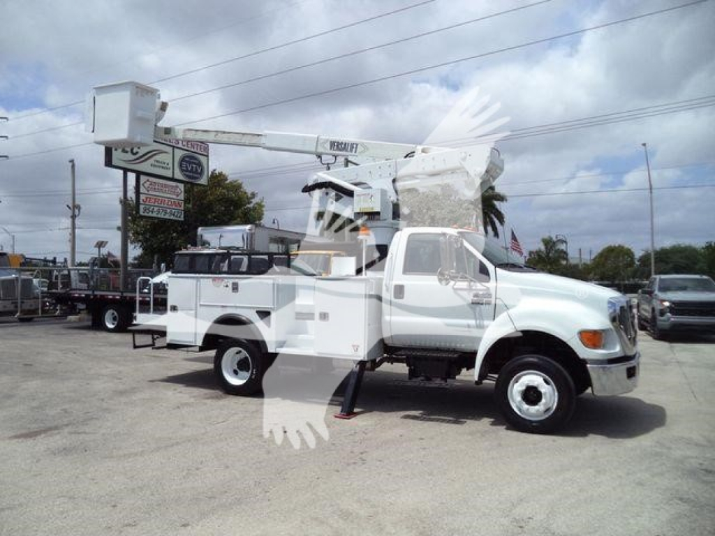 Versalift VST40i bucket crane mounted on a white truck chassis in a dealership lot, side view with extended boom, auxiliary equipment compartments visible