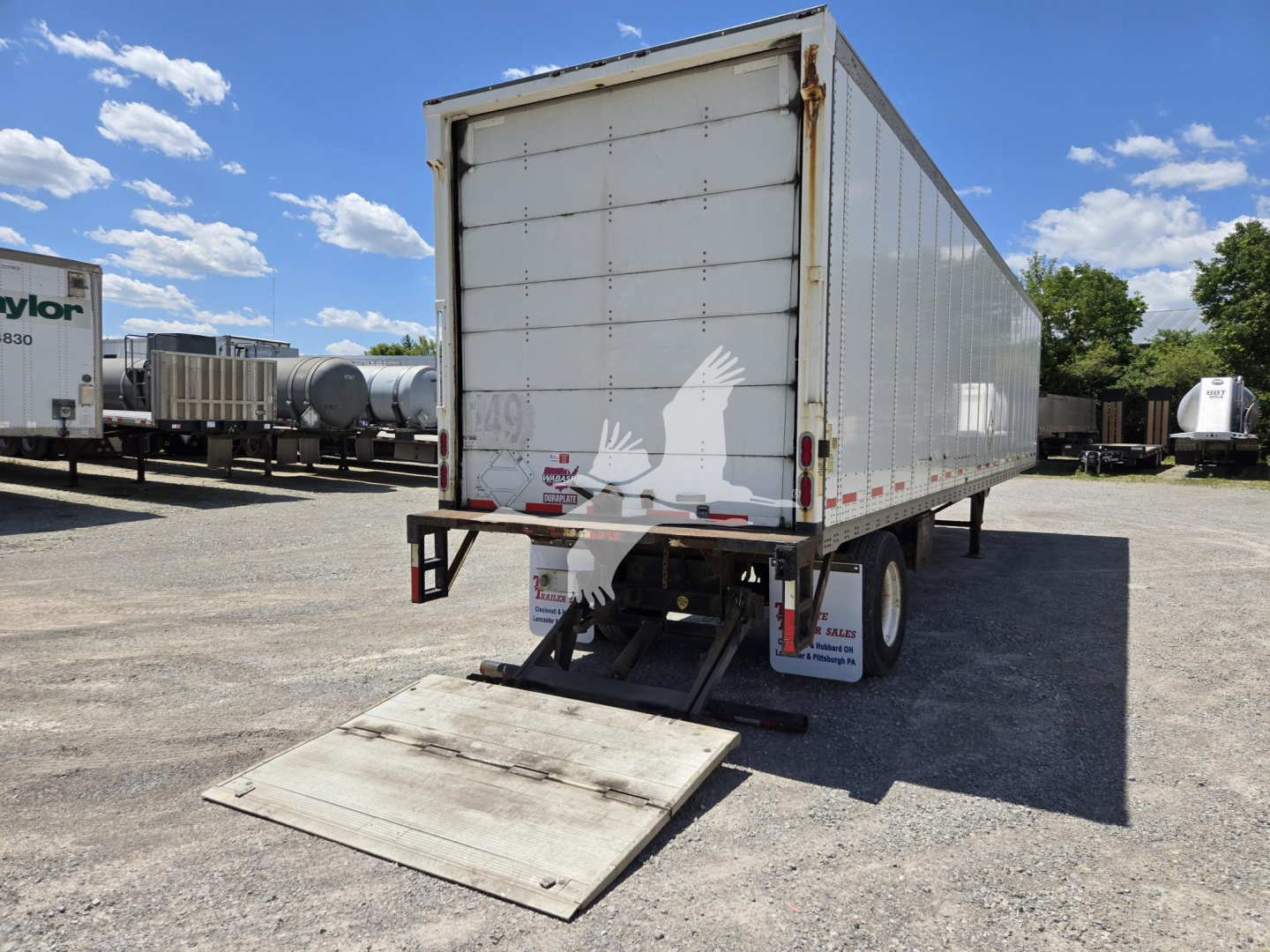 Trailer rear view of a white Wabash box trailer with a lowered ramp in the back, showing the rear doors and underrun guard.