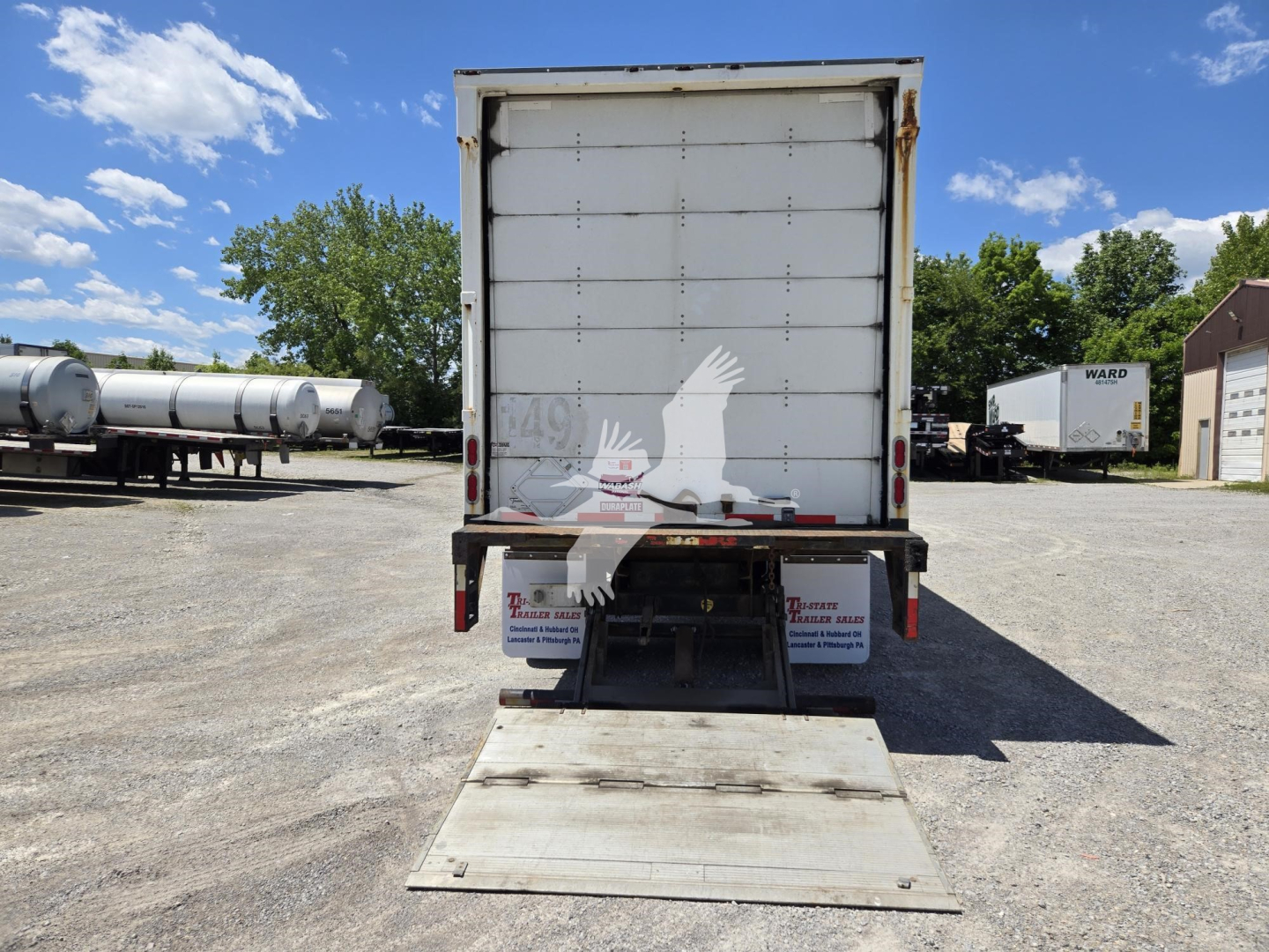 Trailer rear view of a 2014 Wabash van with a lowered ramp/ground door and a closed rear swing door, showing stock area and surrounding trucks.