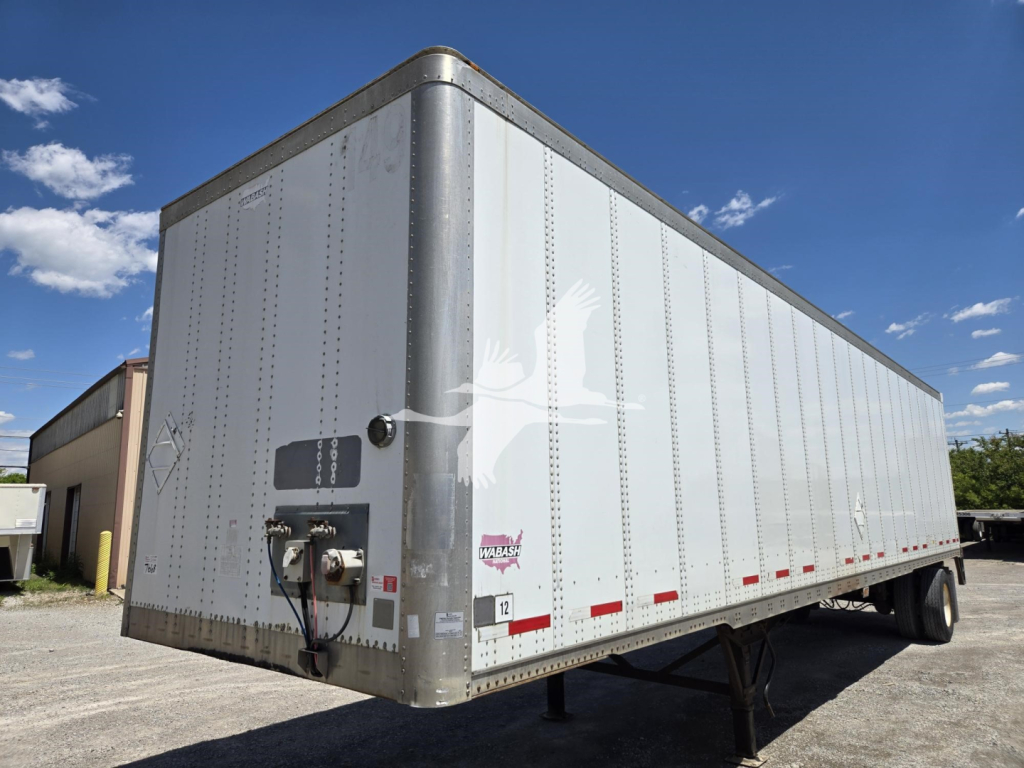 Wabash trailer with silver side panels showing rear jack and hitch, small labeling near front left corner, red reflectors along lower edge.
