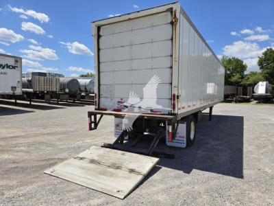 Trailer rear view of a white Wabash box trailer with a lowered ramp in the back, showing the rear doors and underrun guard.