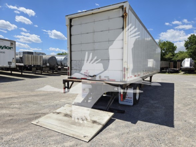 Trailer rear view showing a white enclosed box with a loading ramp extended on a gravel lot; Wabash van trailer, box sides with pattern, clear sky