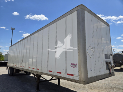 Trailer side view showing a white Wabash van trailer with a bird logo and reflective safety strips, quad rear doors, and landing gear visible under the empty trailer.