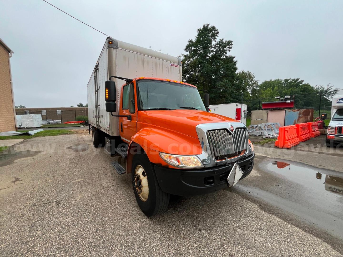 Truck cab view of a bright orange 2004 International 4300SBA with box trailer attached, front grille, and black bumper.