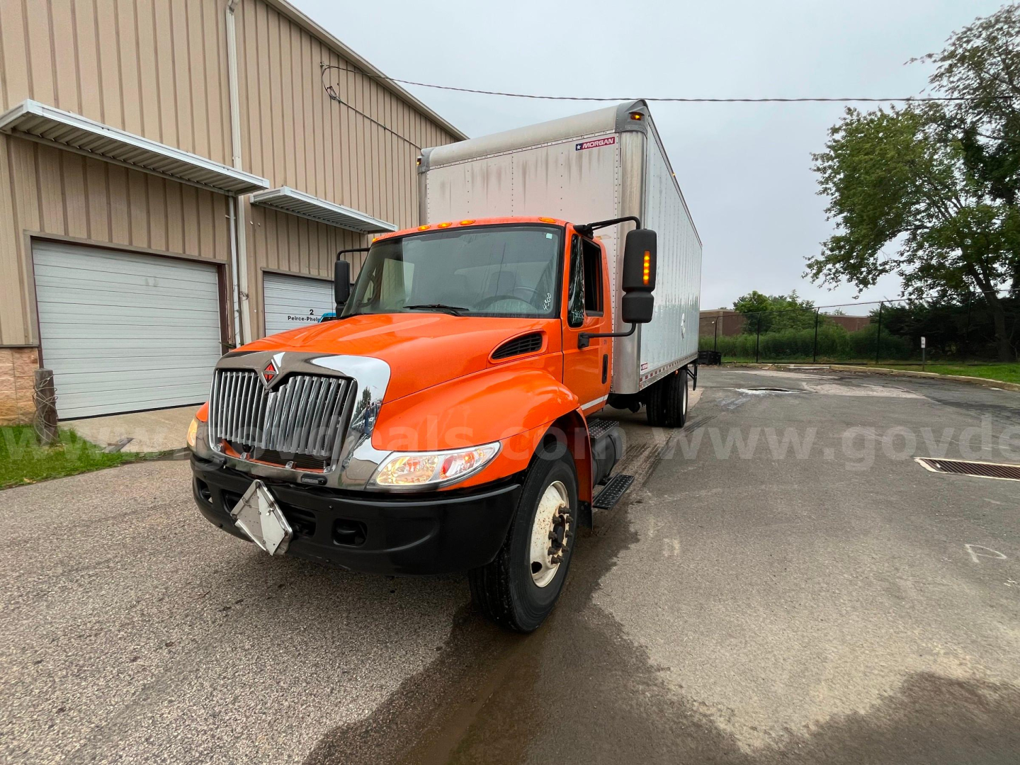 Truck in service orange cab with box body showing front grille and headlights, North American medium-duty truck.