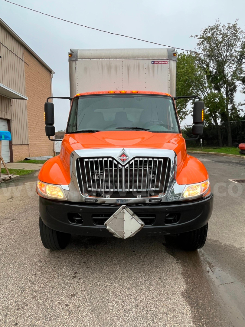 Front view of an orange 2004 International 4300 SBA box truck, chrome grille, large bumper, dual headlights, diamond-shaped front emblem, cargo box behind cab.