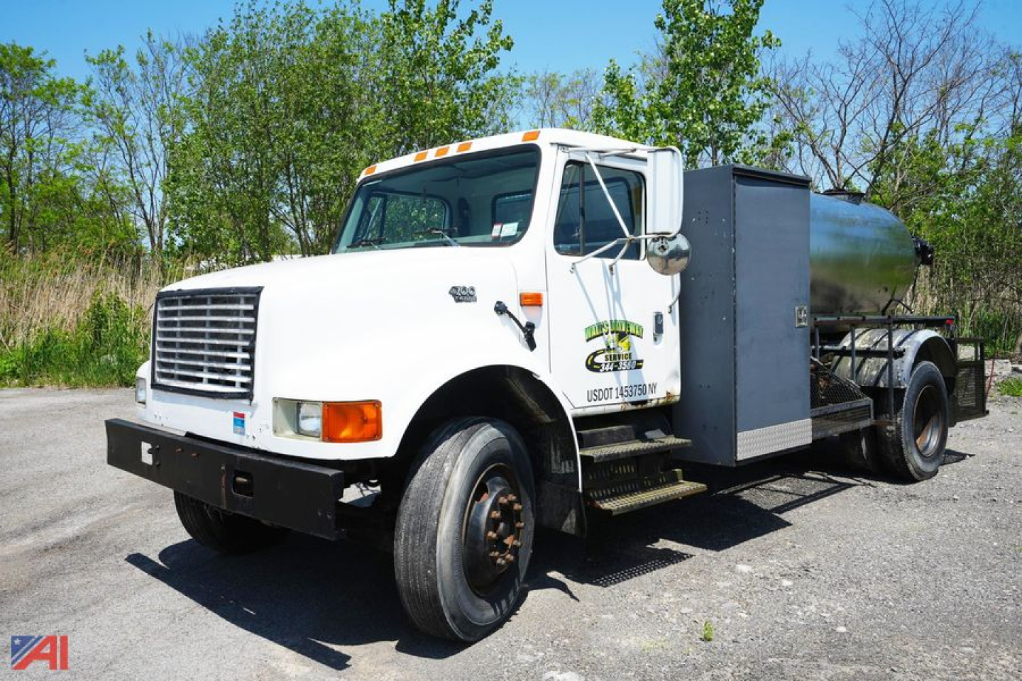 International 4700 1000 gal sealer truck in-service showing front grille, cab, and stainless tank with toolbox.