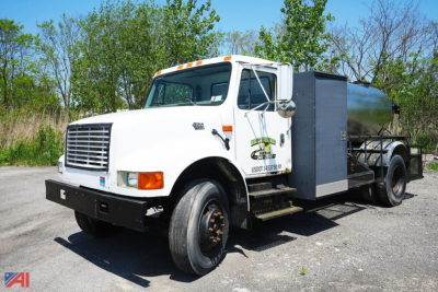 International 4700 1000 gal sealer truck in-service showing front grille, cab, and stainless tank with toolbox.