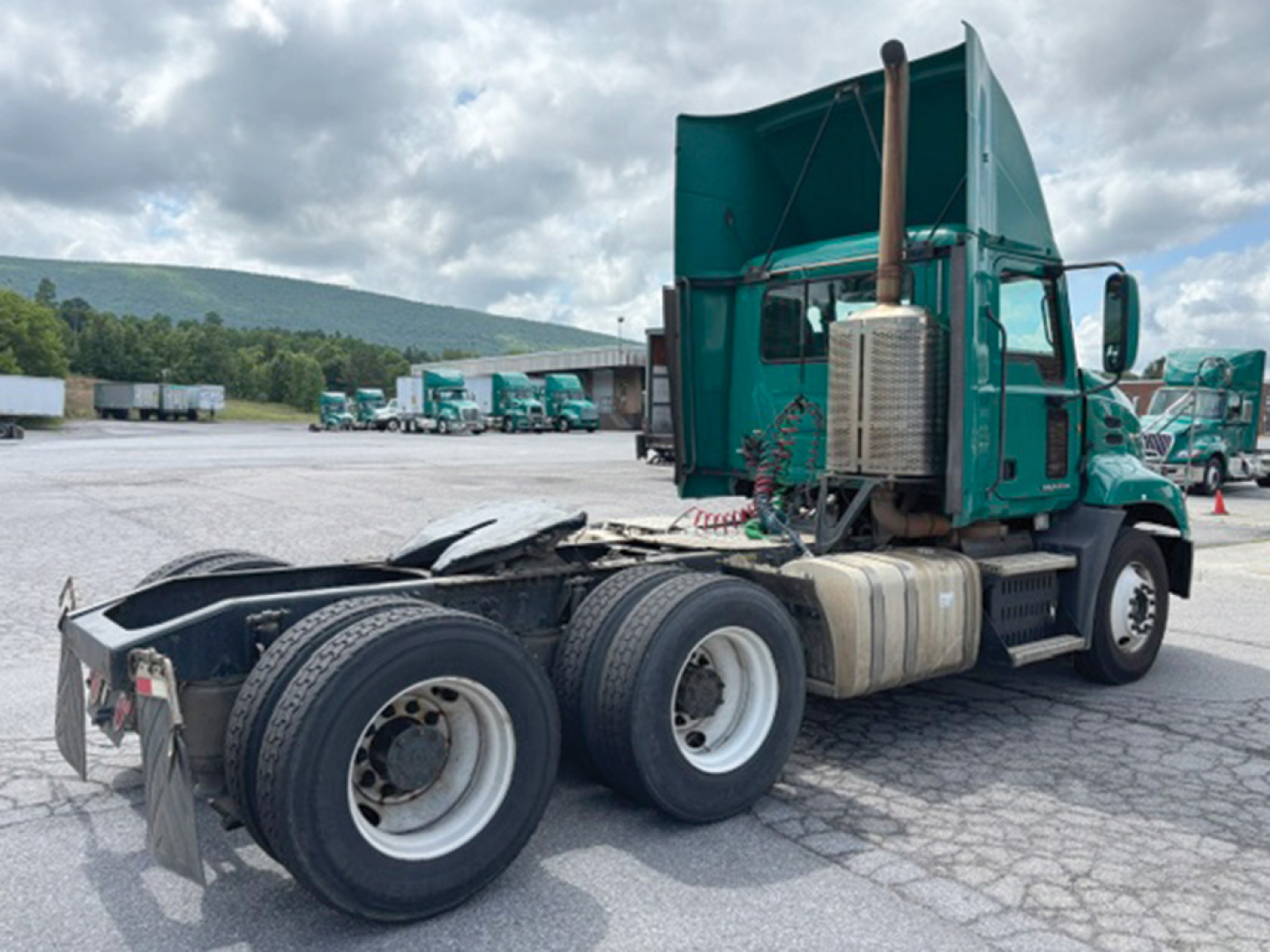 Truck chassis and cab of a 2015 Mack CXU613 with green exterior, dual rear axles, exposed exhaust stack, and fuel tanks.