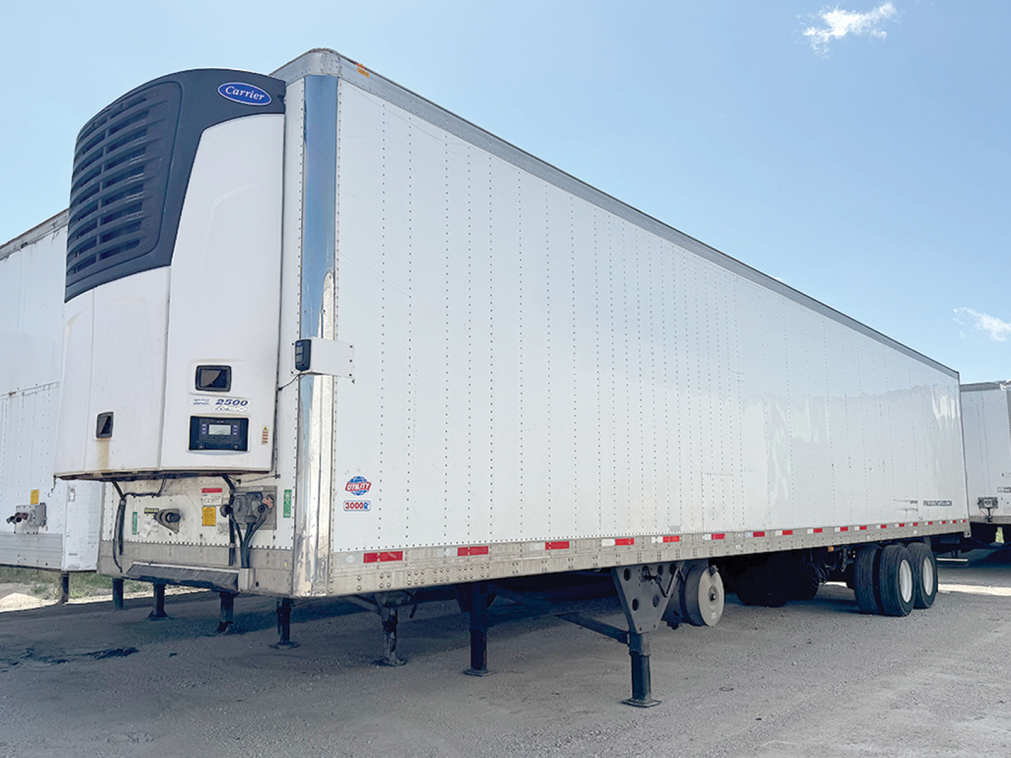 Utility 3000R semi-trailer with a large white refrigerated body and a Carrier refrigeration unit at the front, aluminum side panels, and tandem rear wheels.