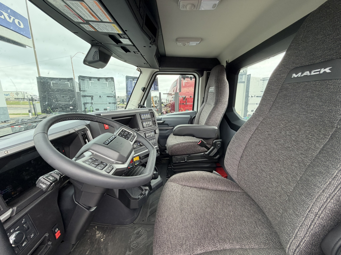 Mack AN64T truck cockpit interior showing steering wheel, dashboard, driver seat, and passenger seat with Mack branding on headrest.