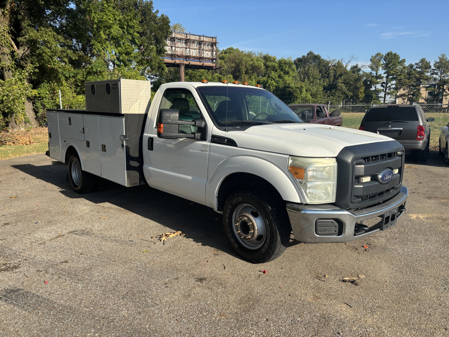 Ford F-350 cab and chassis utility truck in a parking lot, white with utility box and diamond-plate compartments.