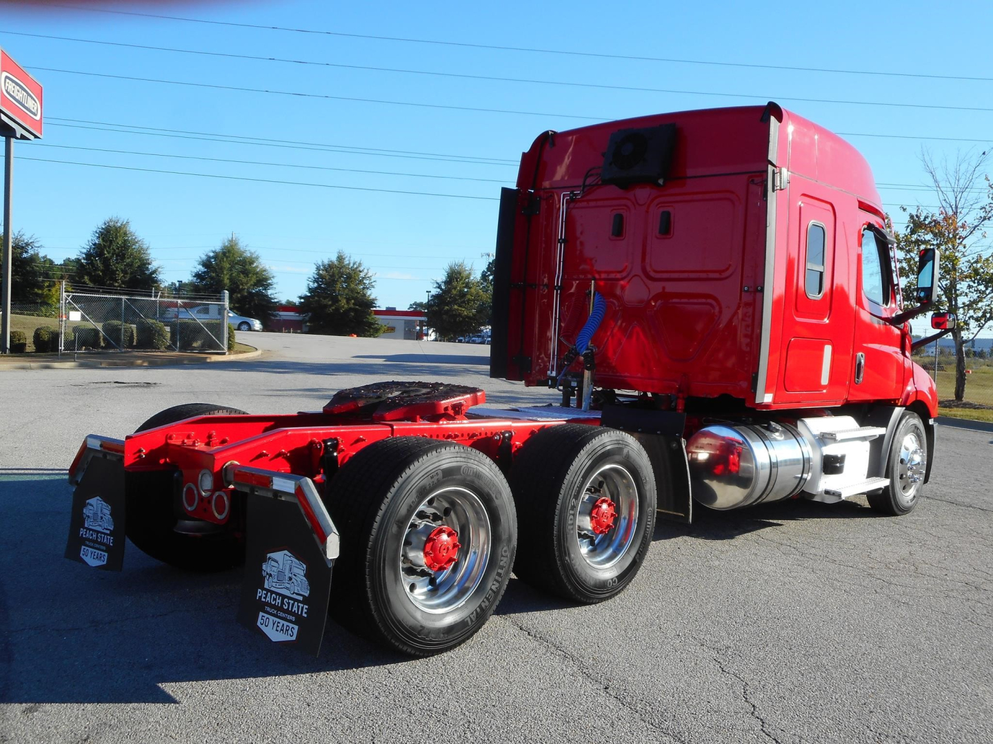 Truck chassis in a red Freightliner Cascadia 116 tractor with three rear axles and chrome fuel tanks, showing red cab and black tires.