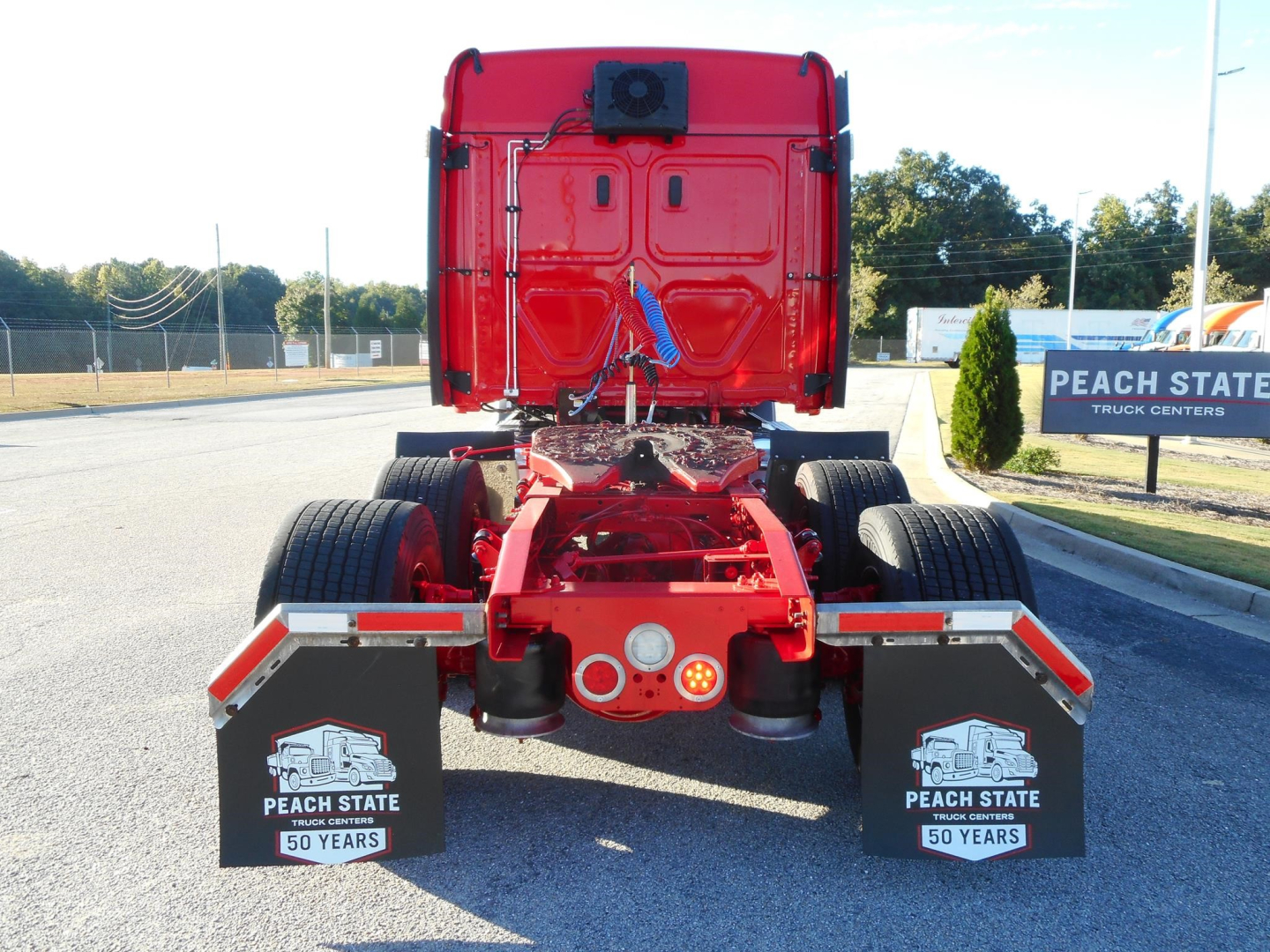 Rear view of a red Freightliner Cascadia tractor showing chassis and rear fenders with Peach State Truck Centers mudflaps and a blue strap.