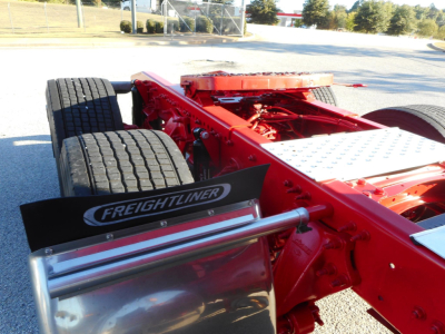 Freightliner Cascadia chassis and rear section showing red frame, dual rear axles, metal diamond-plate step, and Freightliner mudguard emblem.