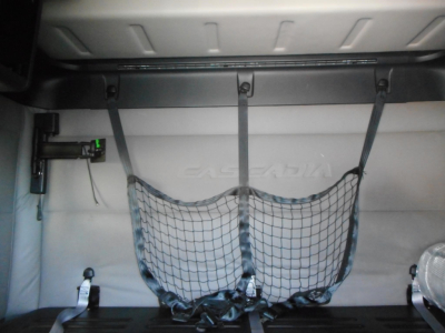 Freightliner Cascadia 116 sleeper cab interior view with cargo net and rear side panel, showing light gray interior and straps.