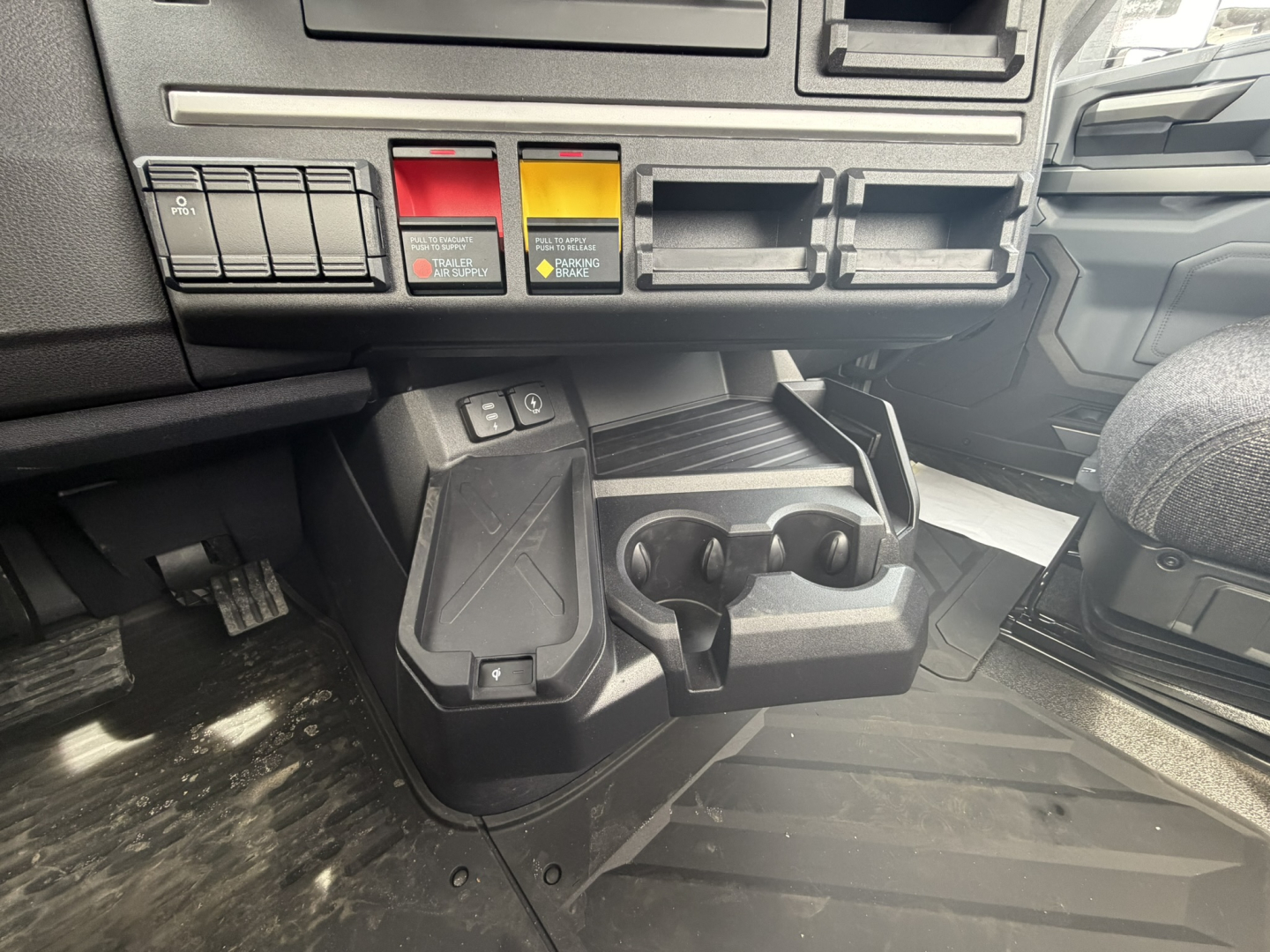 Cab interior showing control switches and dual cup holders in a 2027 Mack AN64T truck dashboard area.