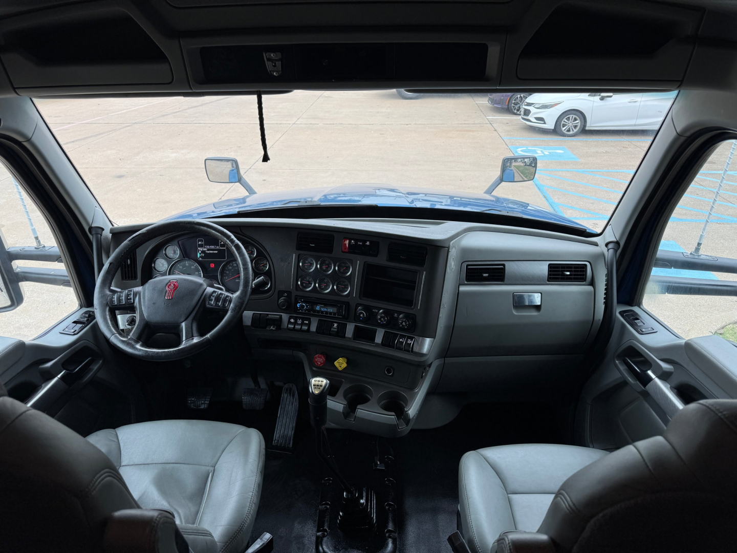 Cab interior of a 2019 Kenworth T880, steering wheel on left, dashboard with gauges, center console, two front seats, gear shifter, and window view.