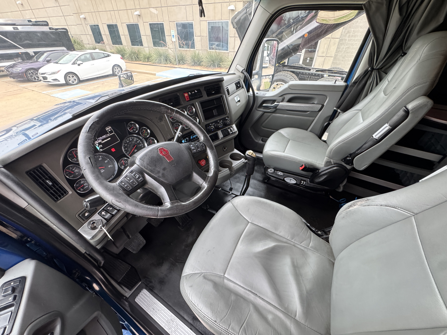 Kenworth T880 cab interior showing steering wheel, dashboard, and gray seats.